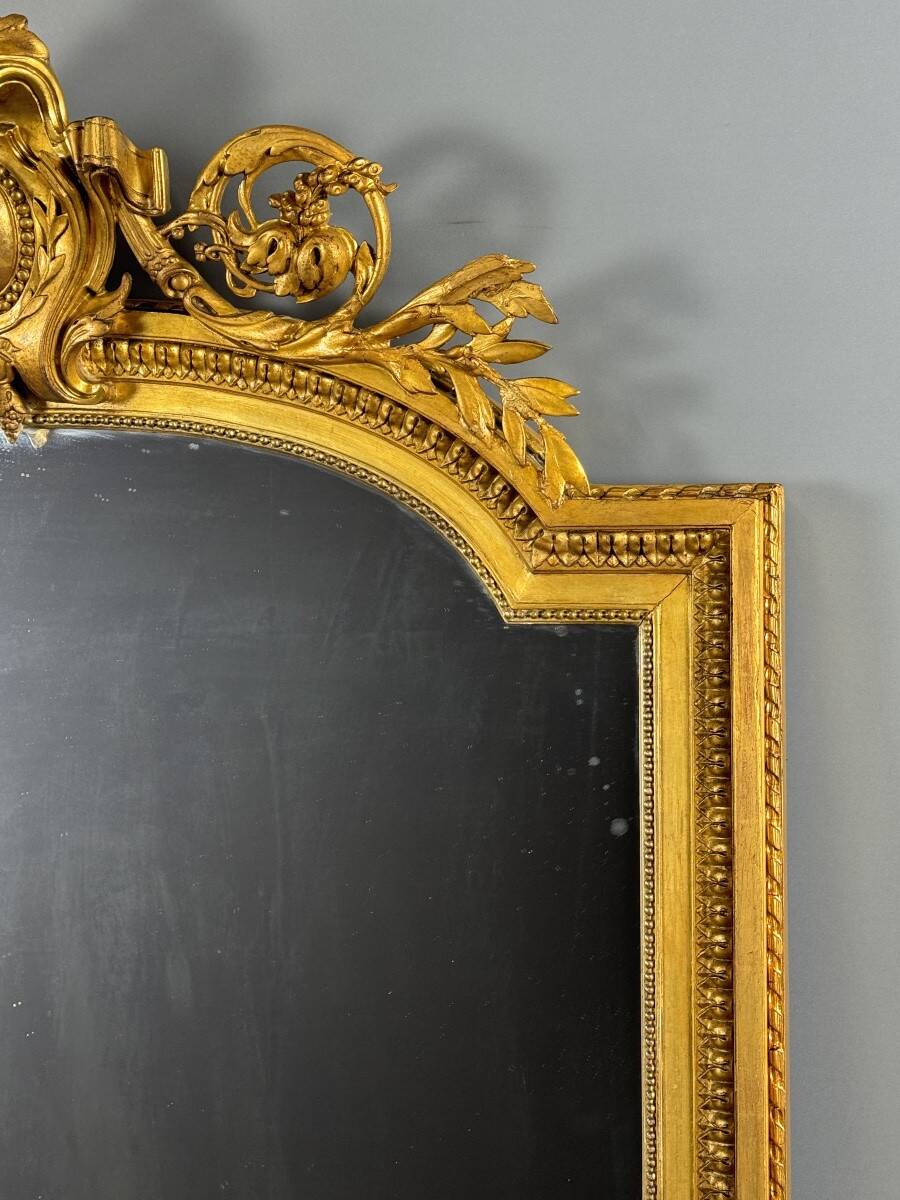 Large antique gilded wooden mirror in Louis XVI style with a sculpted pediment, 19th century.