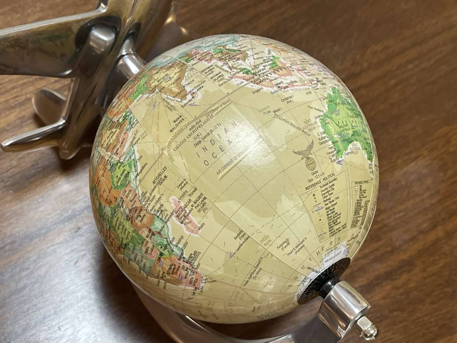 1960s terrestrial globe on a chrome stand with a plane flying over it.