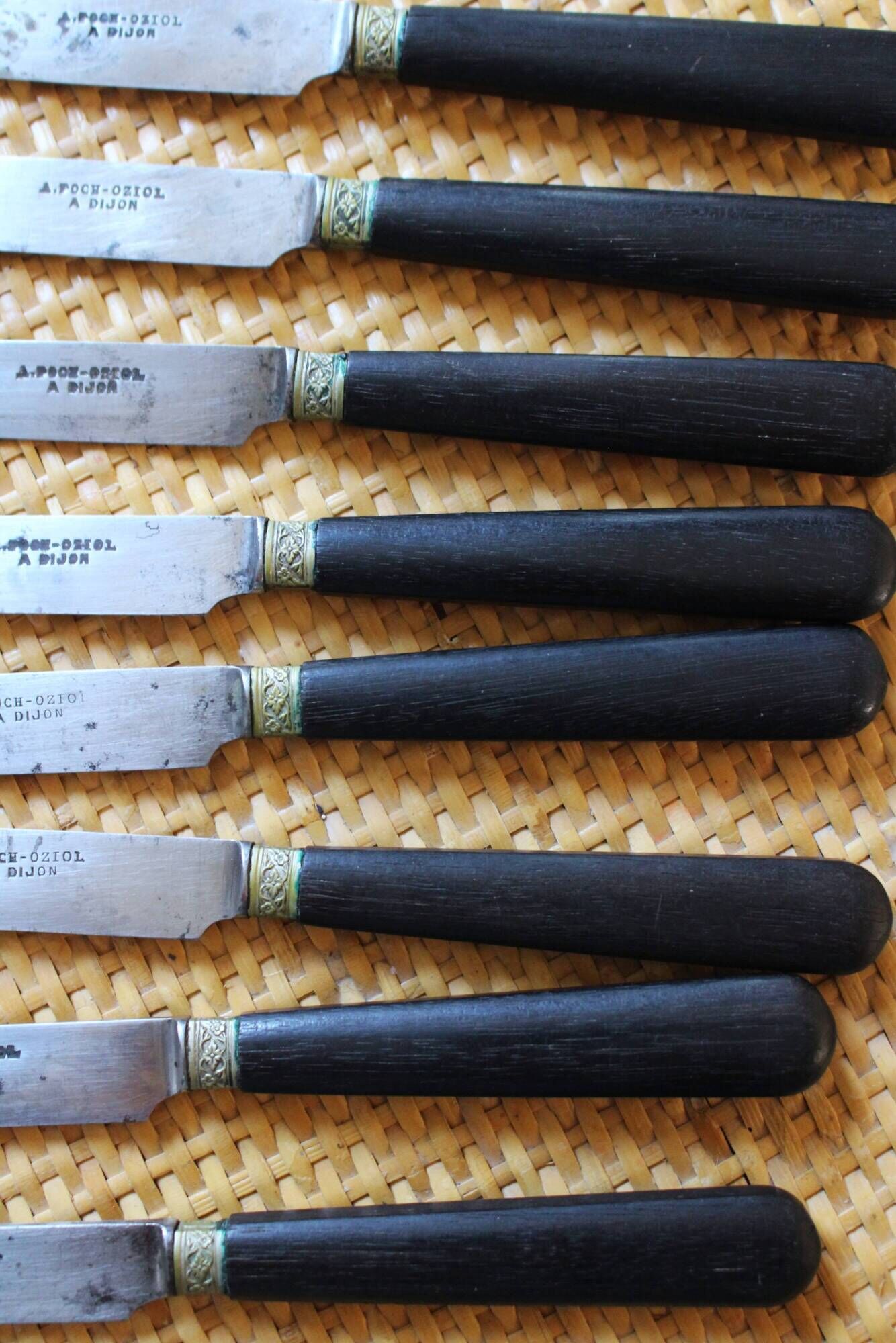 A set of 8 knives with black wooden handles and bolsters.