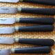A set of 8 knives with black wooden handles and bolsters.
