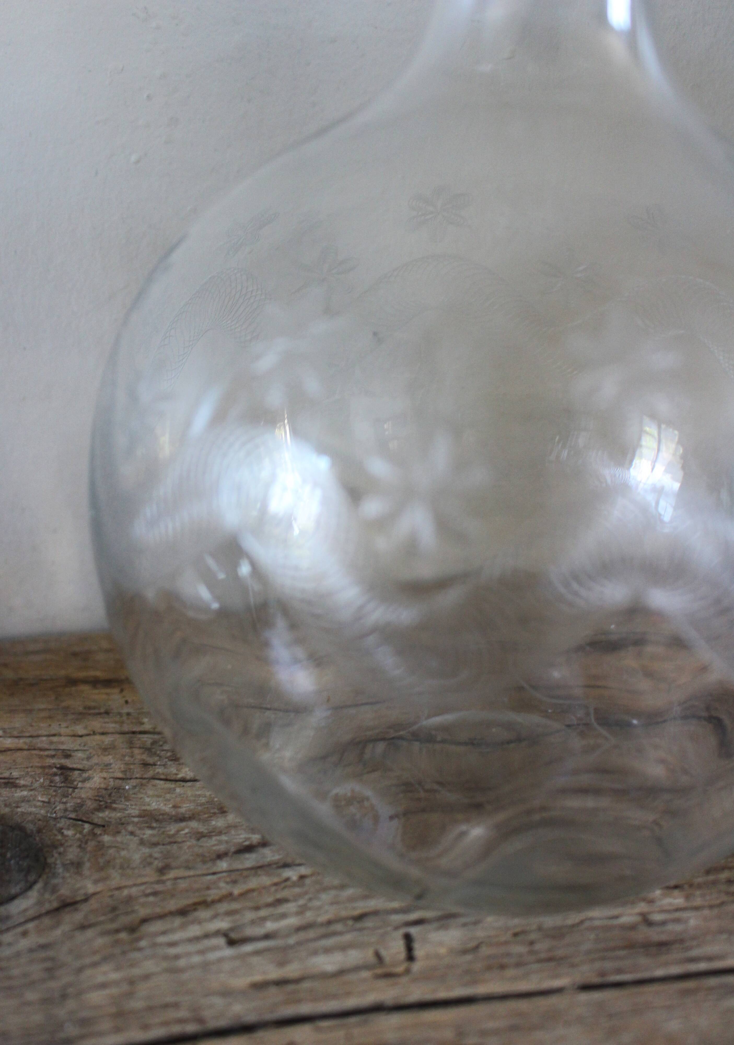 Antique glass carafe with a round belly and floral neck.