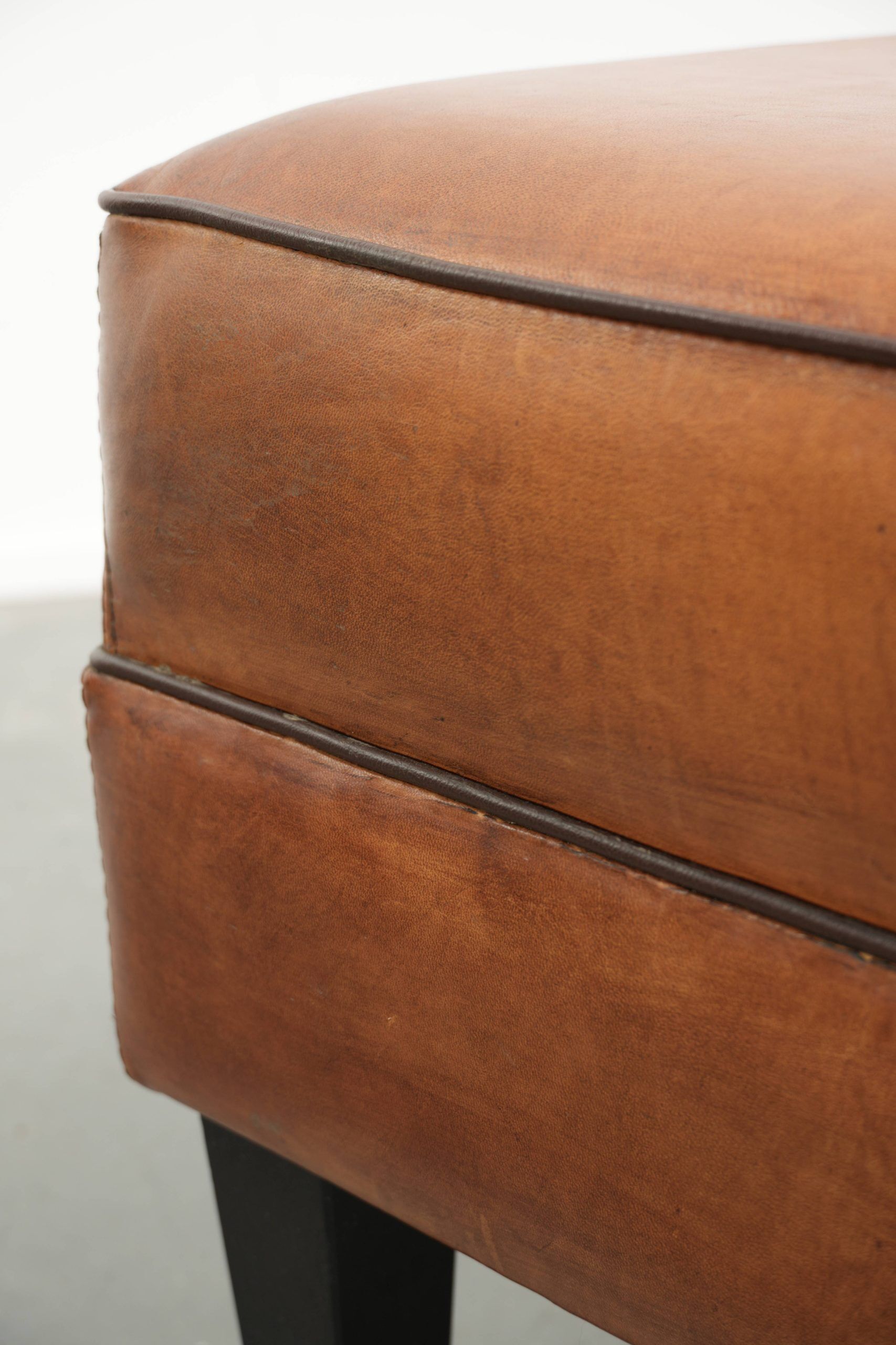 Handy sheepskin ottoman with warm colours finished with black piping