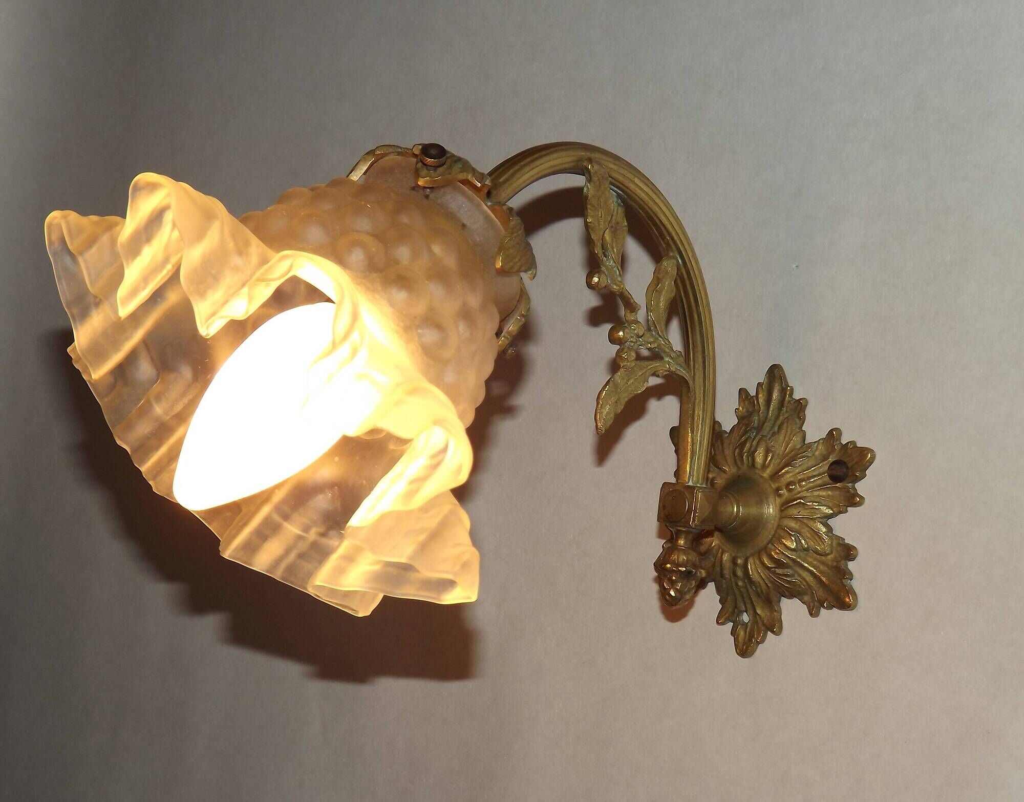 Simple wall sconce in French Art Nouveau bronze with a white glass shade featuring patterns.