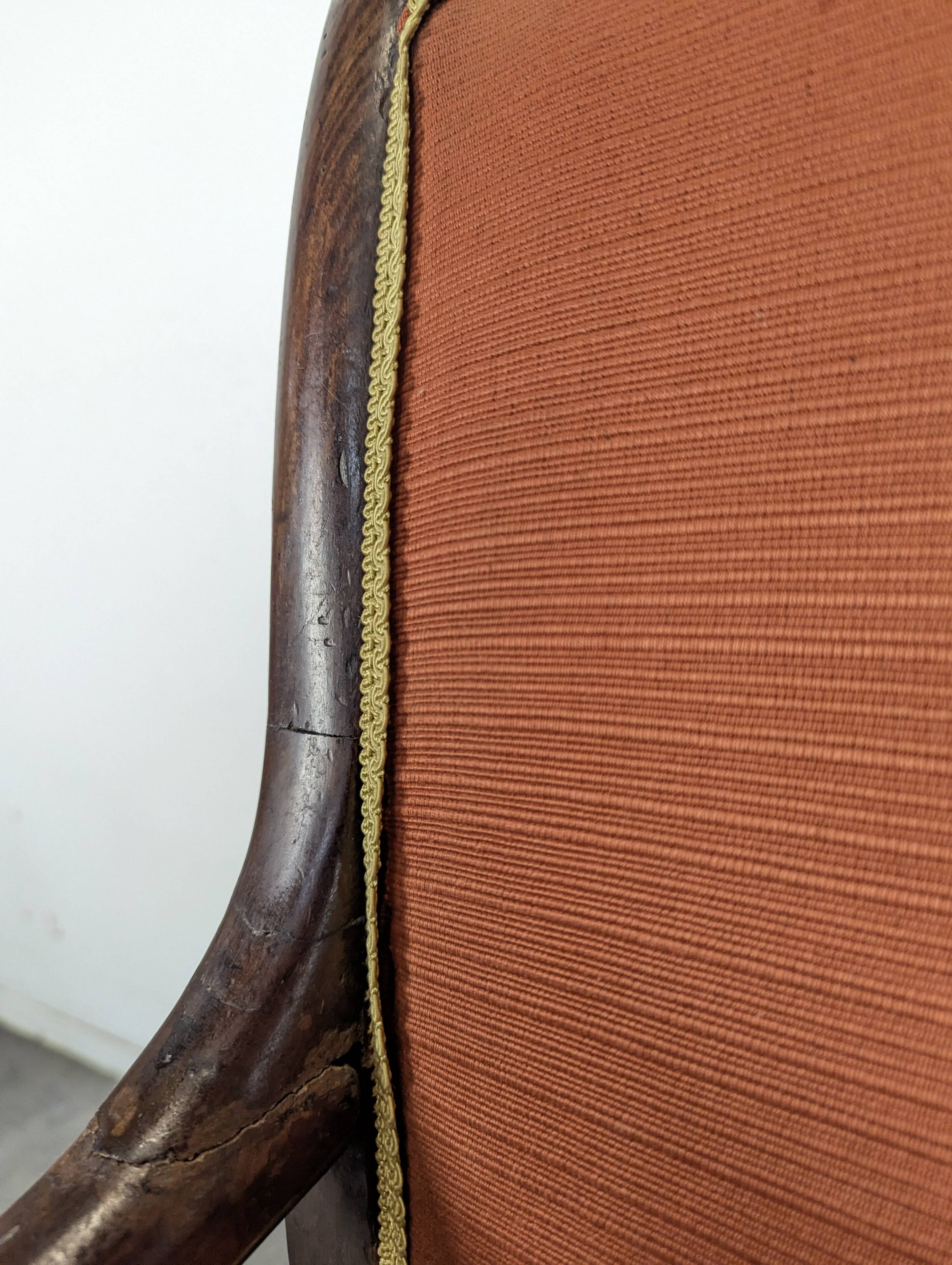 Restoration armchair in mahogany with cross arms and orange fabric.