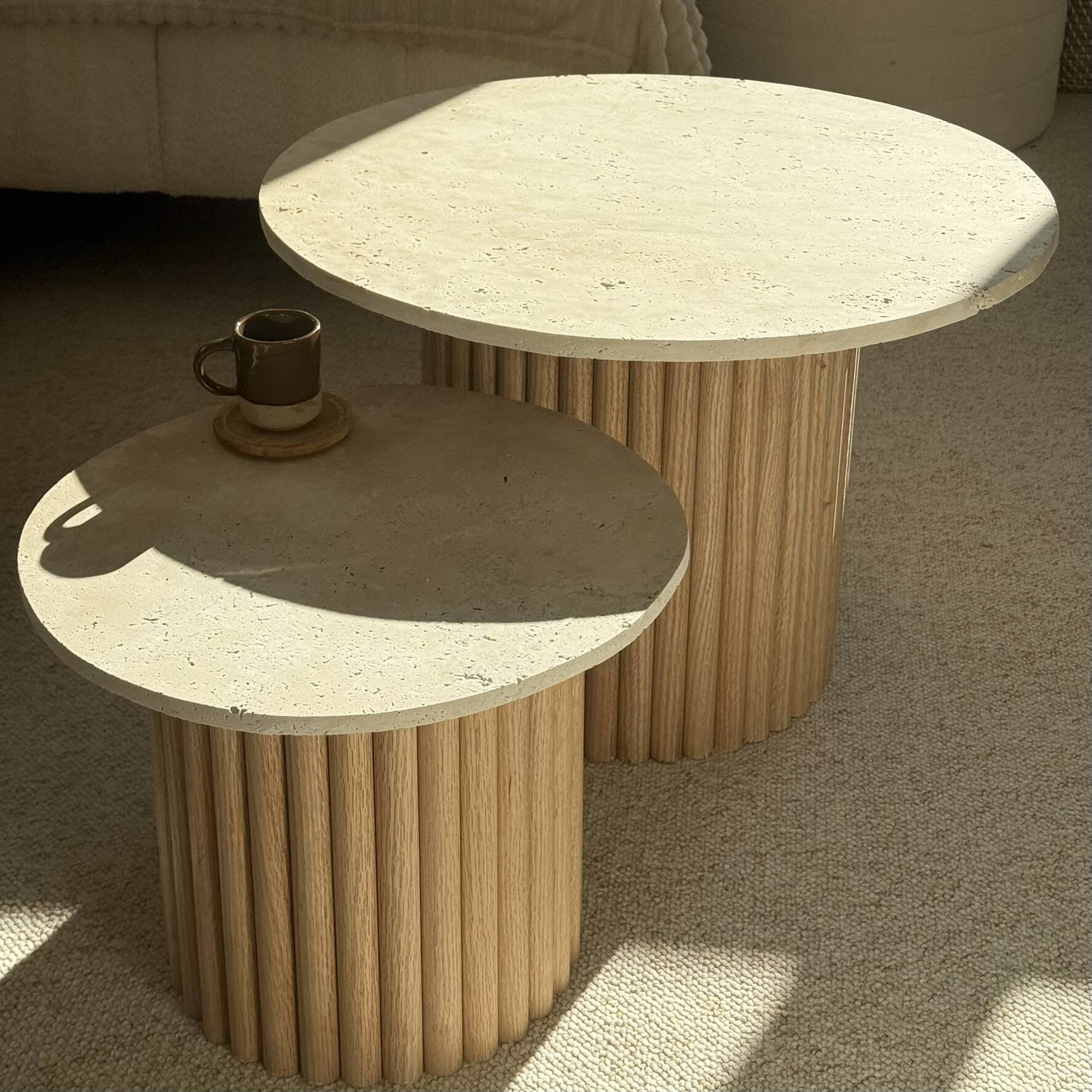 Round nesting coffee table in travertine and raw fluted wood.