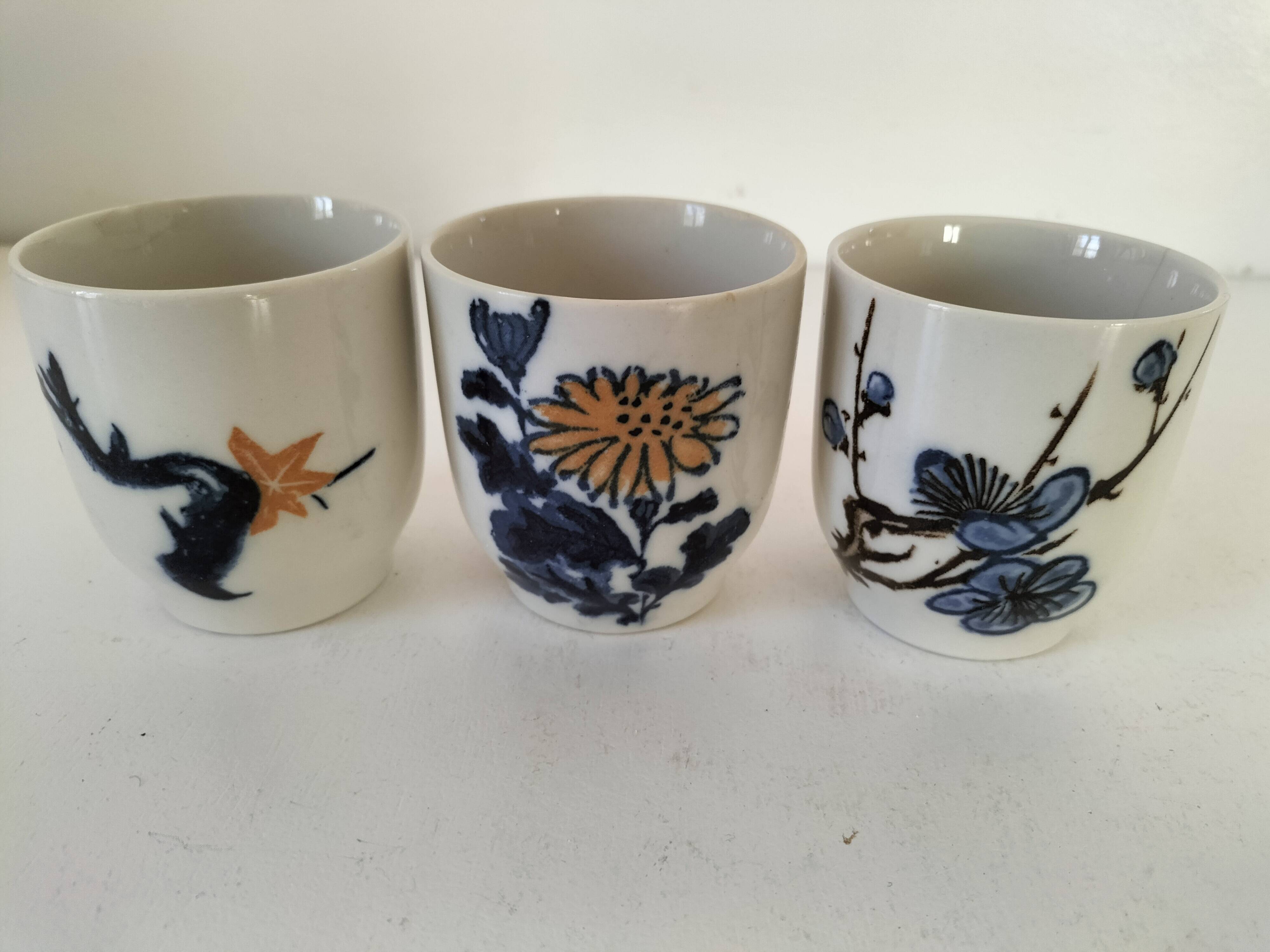 Set of three hand-painted porcelain cups with floral patterns.