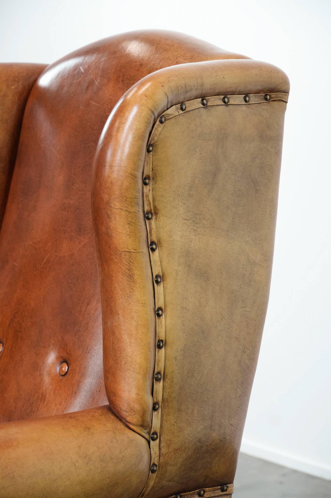 Large sheepskin wingback chair with black piping and decorative nails
