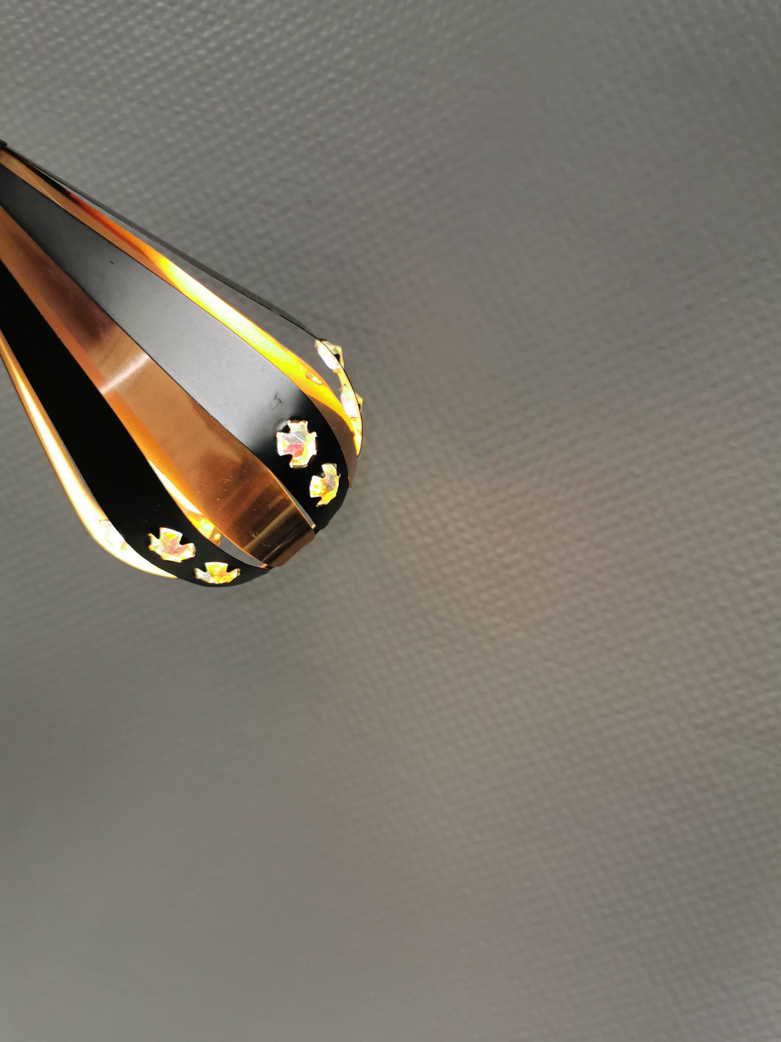 A teardrop-shaped pendant lamp made of copper, black metal, and prisms.