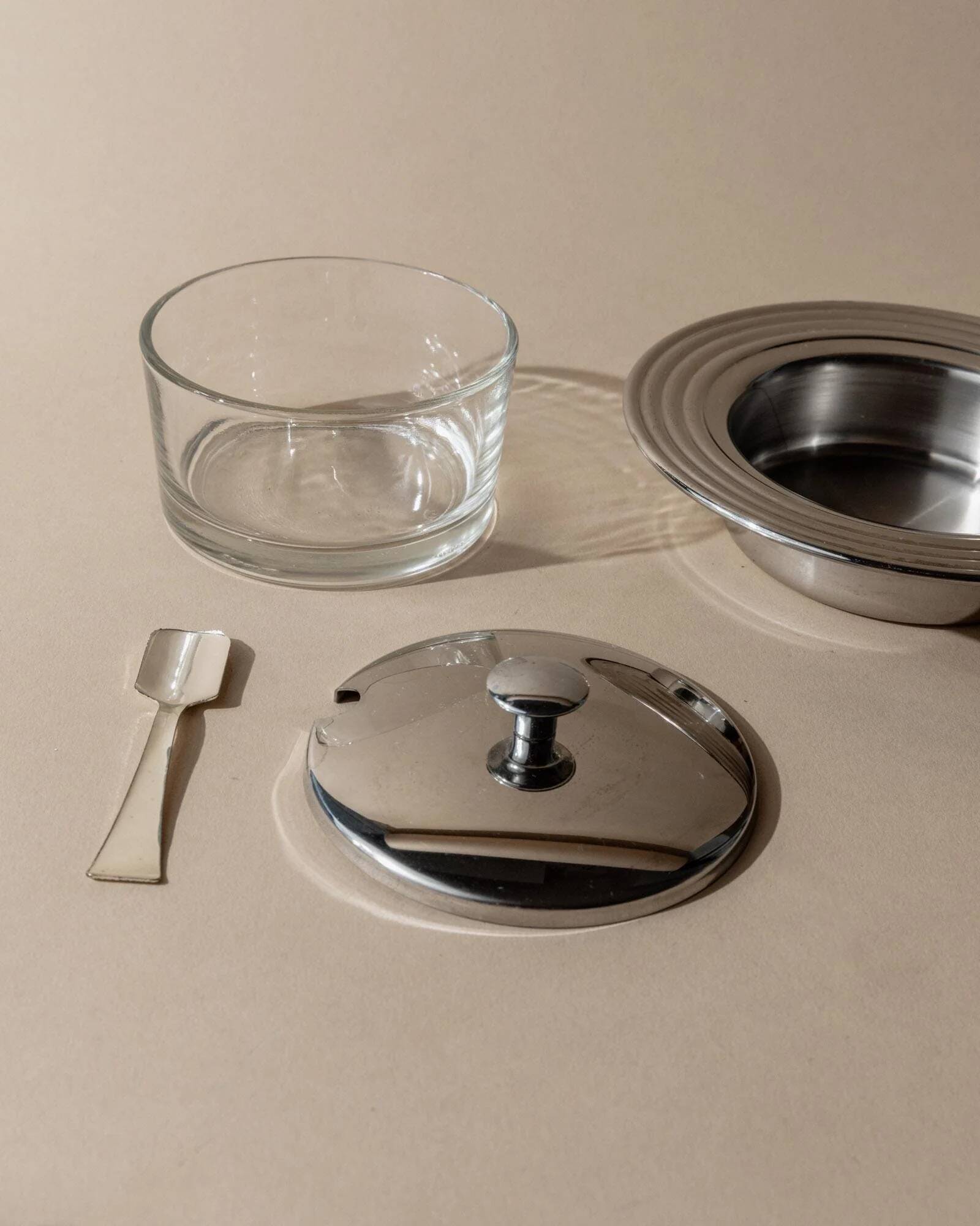 Vintage 1970s condiment pot made of glass and stainless steel with a lid, complete with a matching spoon.