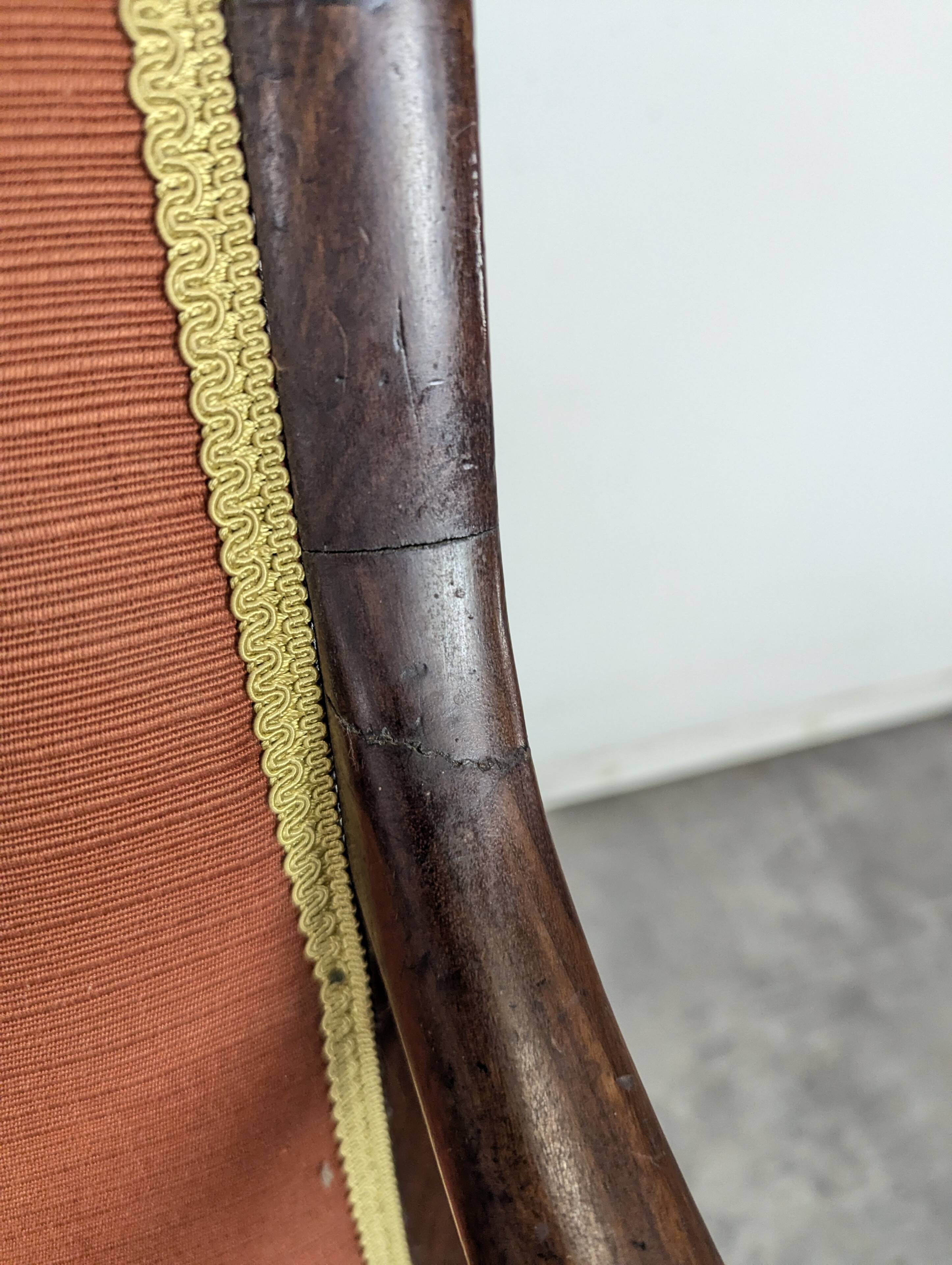 Restoration armchair in mahogany with cross arms and orange fabric.