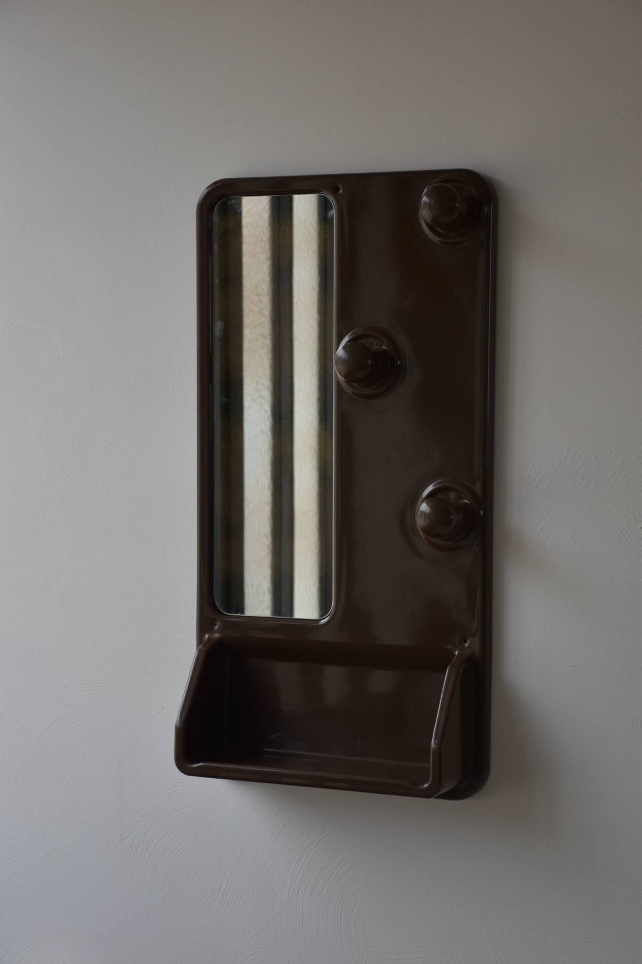 Wall mirror in moulded plastic with hooks and shelf.
