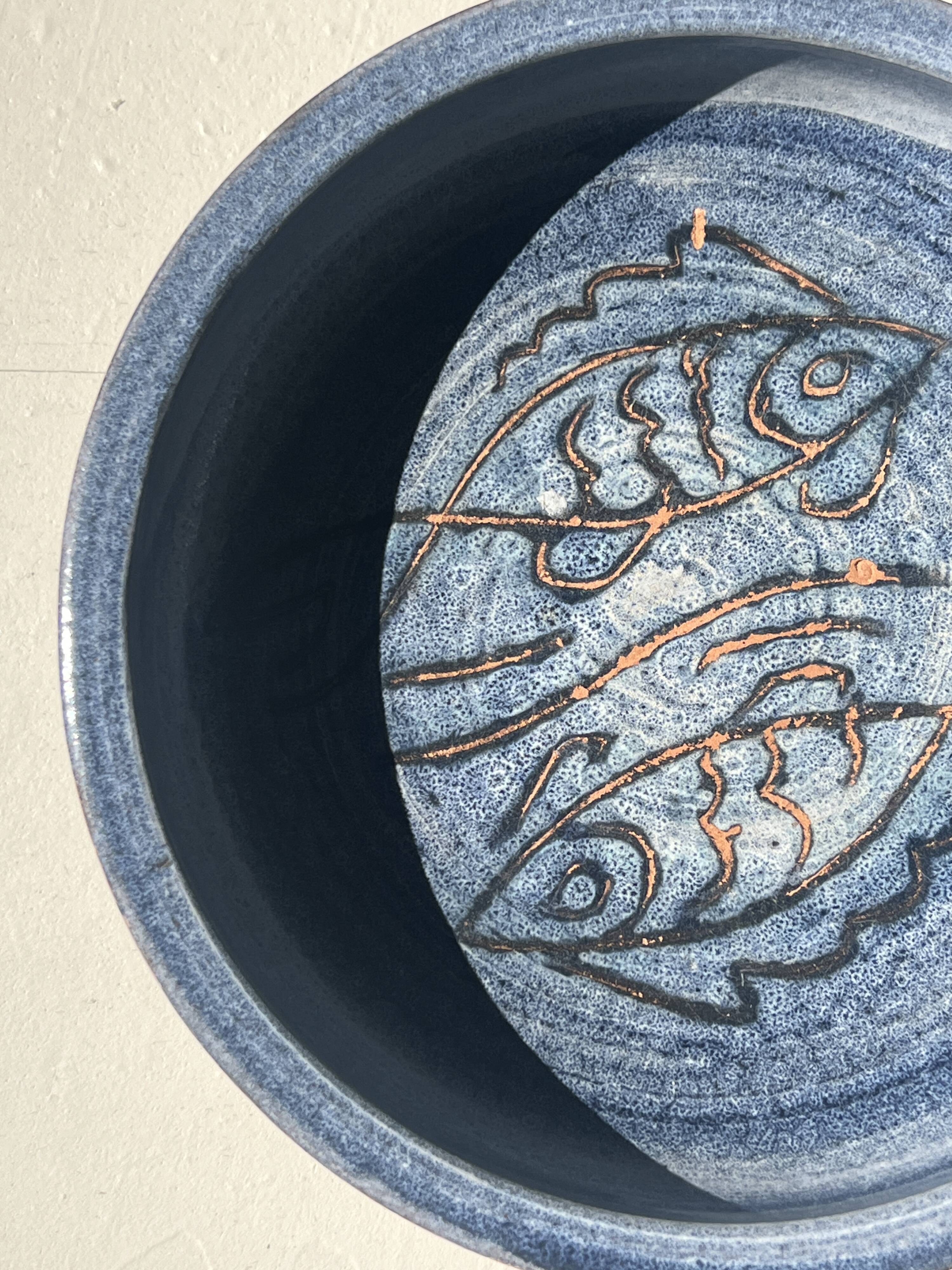 Glazed blue ceramic bowl with stylised fish decoration.