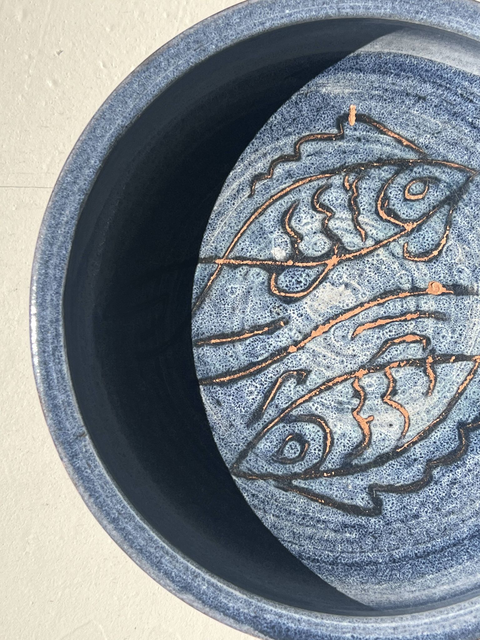 Glazed blue ceramic bowl with stylised fish decoration.