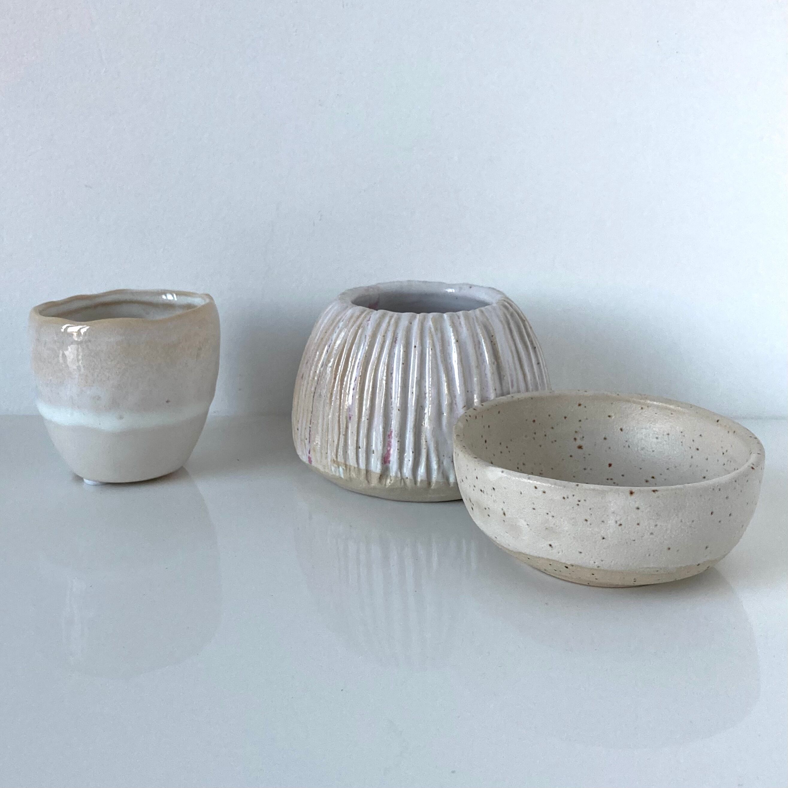 Meeting of three artist's ceramic objects including two pots and a cream covered bowl