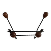 Wall-mounted coat rack in wrought iron with turned wooden knobs.