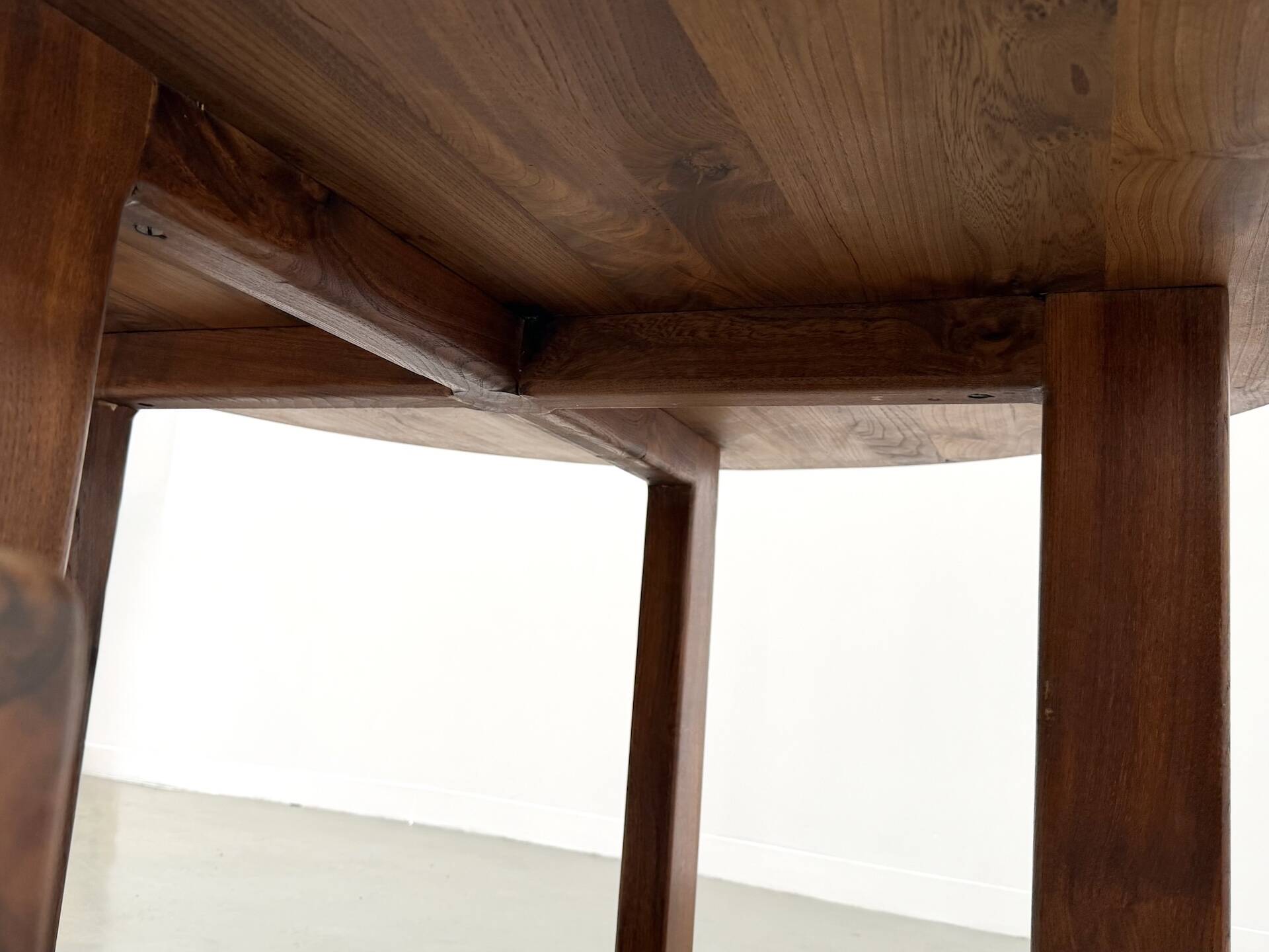 Modernist round table in solid elm, crossed legs.