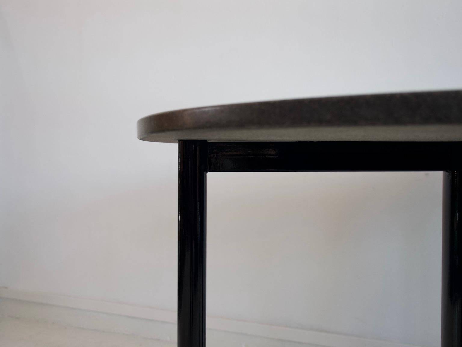 Round dining table in black lacquered metal with a granite top.