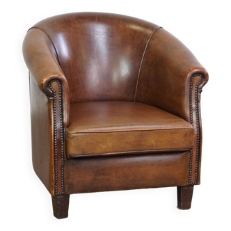 Fauteuil club en cuir de mouton discret et soigné avec coussin d'assise fixe de couleur cognac foncé et profond