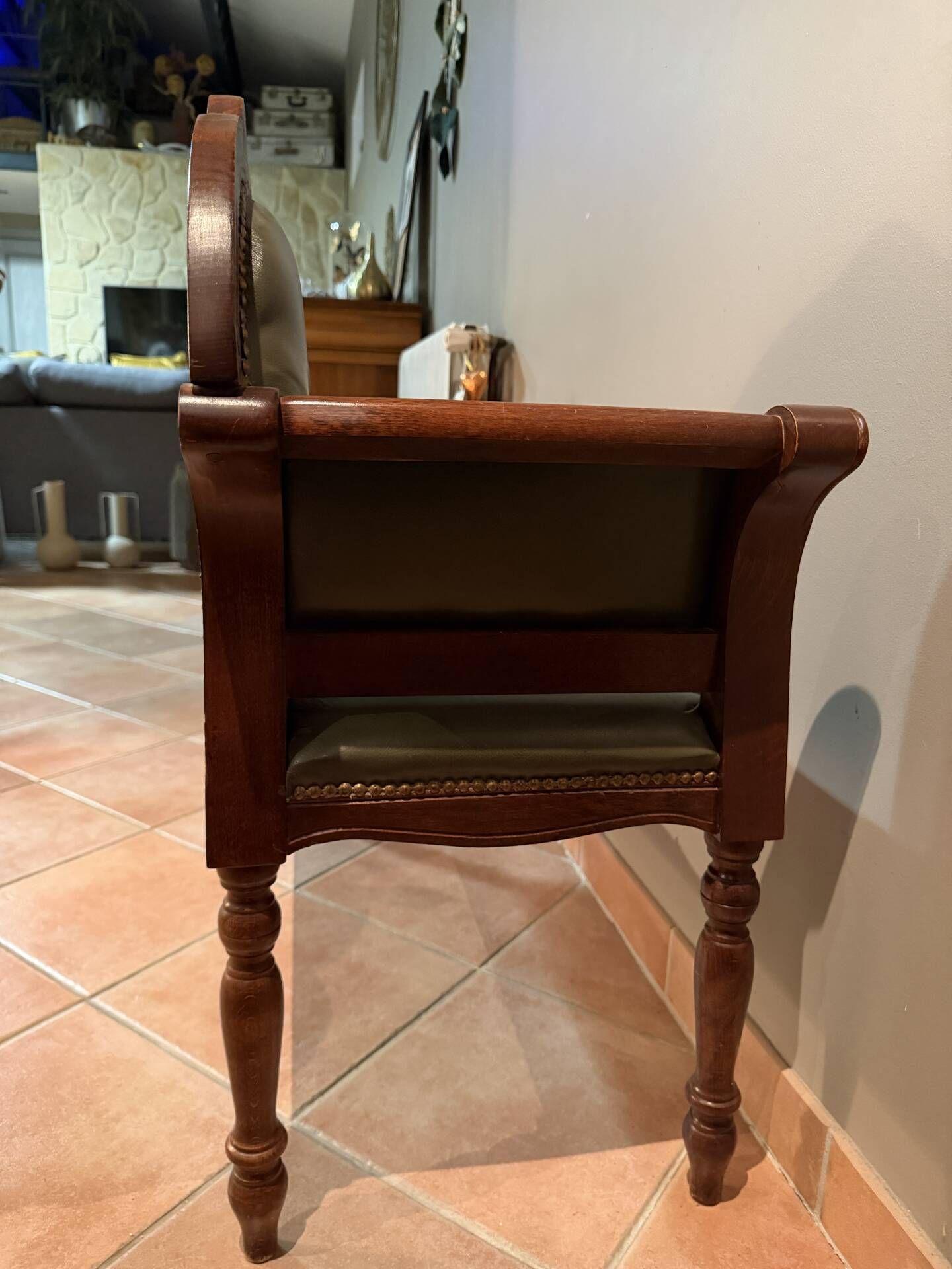 Antique carved wooden bench with green upholstered seat and backrest.