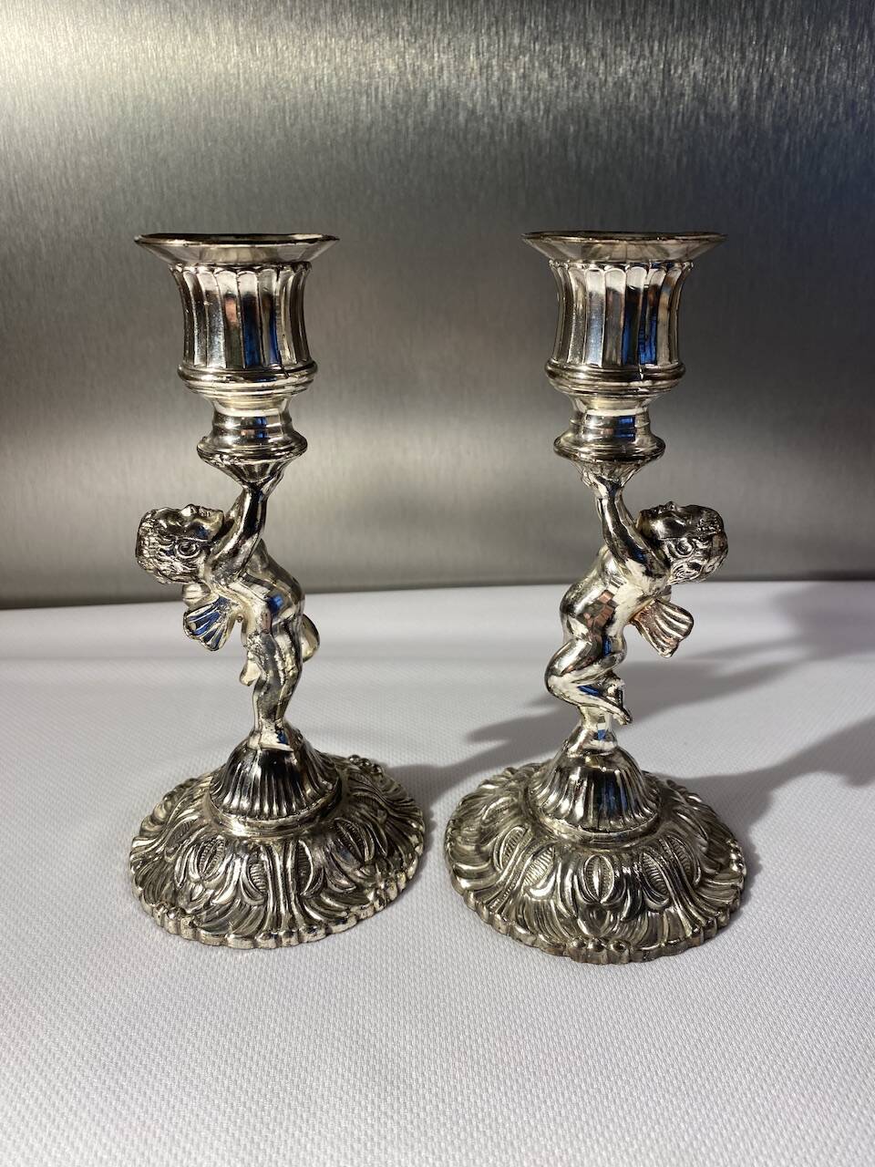 Two silver-plated metal candlesticks decorated with cherubs, 20th century