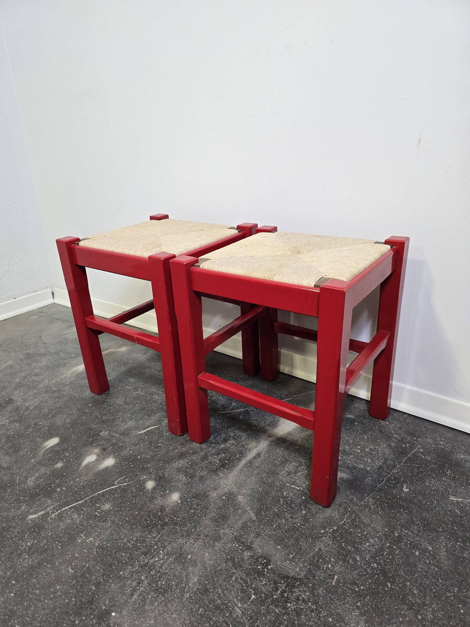 Red wooden stool with a woven straw seat.