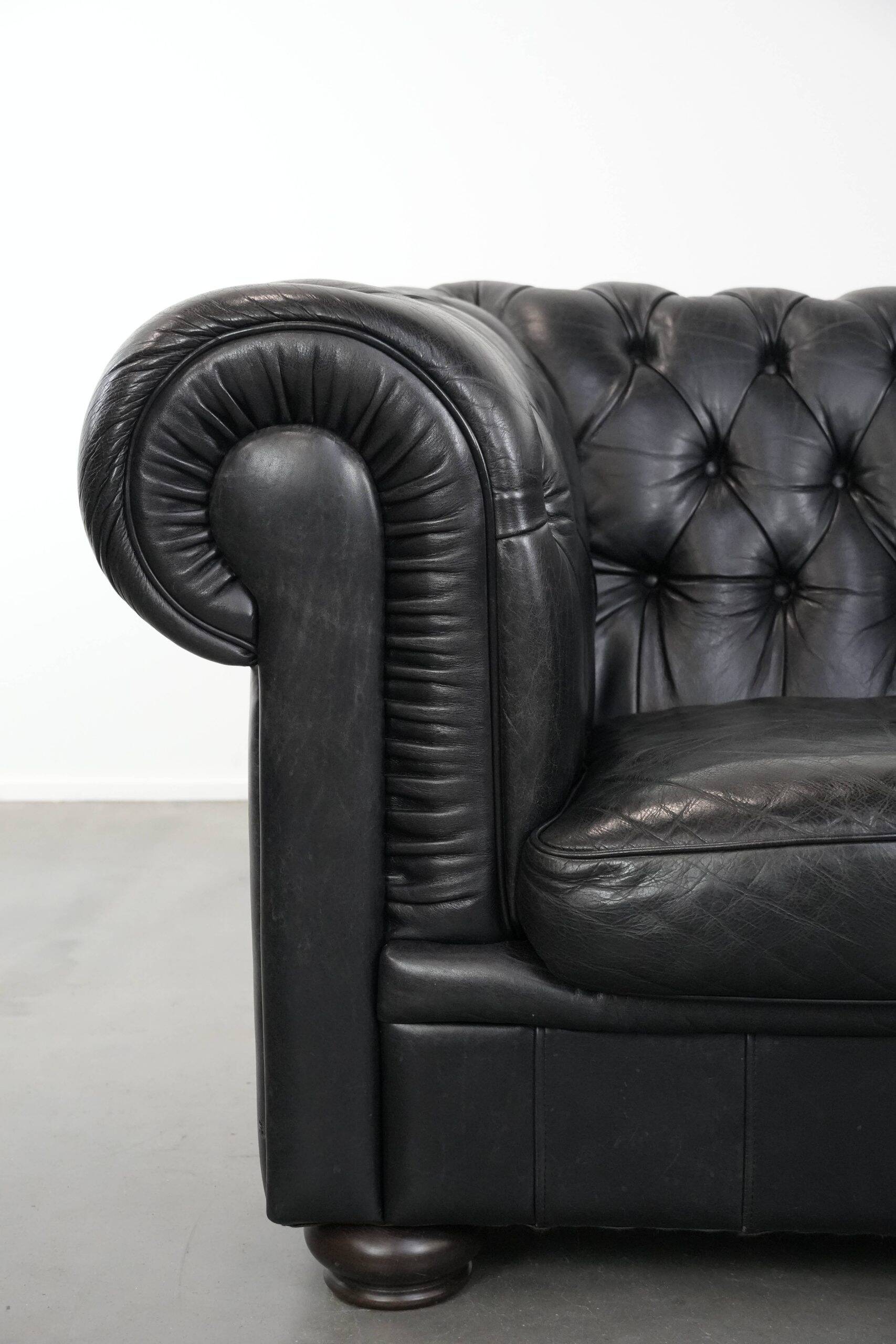 Ensemble composé d'un canapé chesterfield noir, d'un fauteuil et d'un pouf.