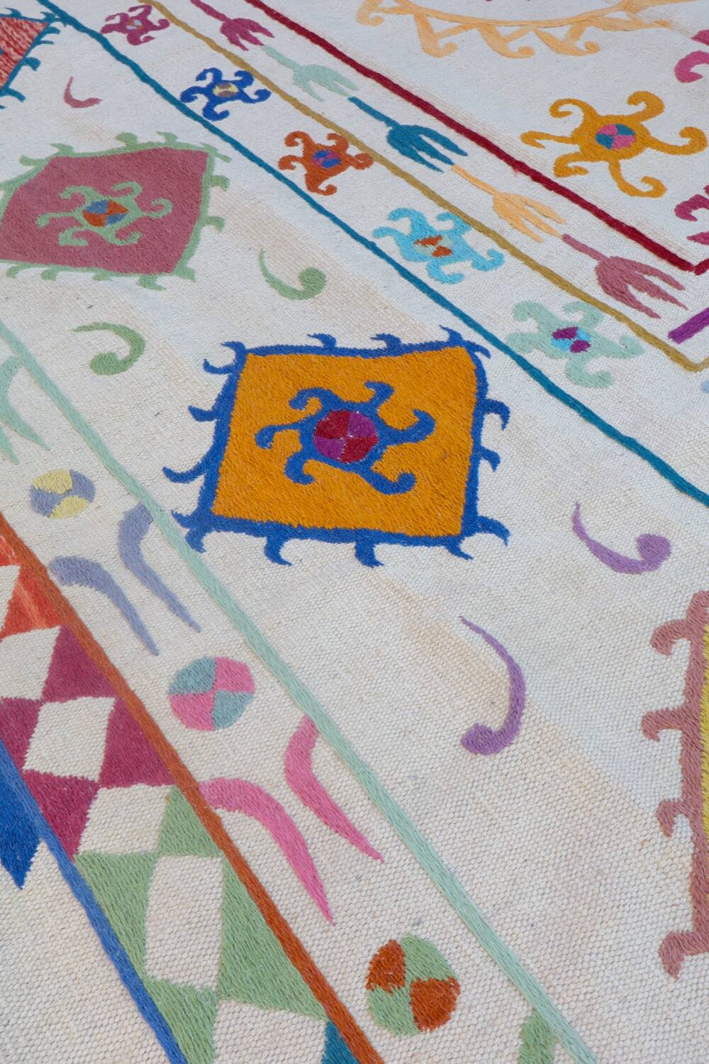 White suzani kilim rug with multi-colored embroidered patterns
