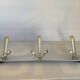 Stainless steel coat rack with three double hooks.