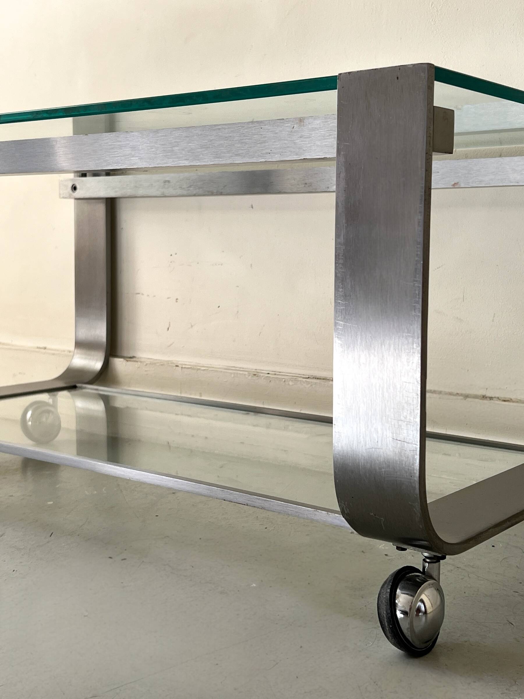 Brushed chrome coffee table with glass, 2 tiers on wheels, 1970s design.