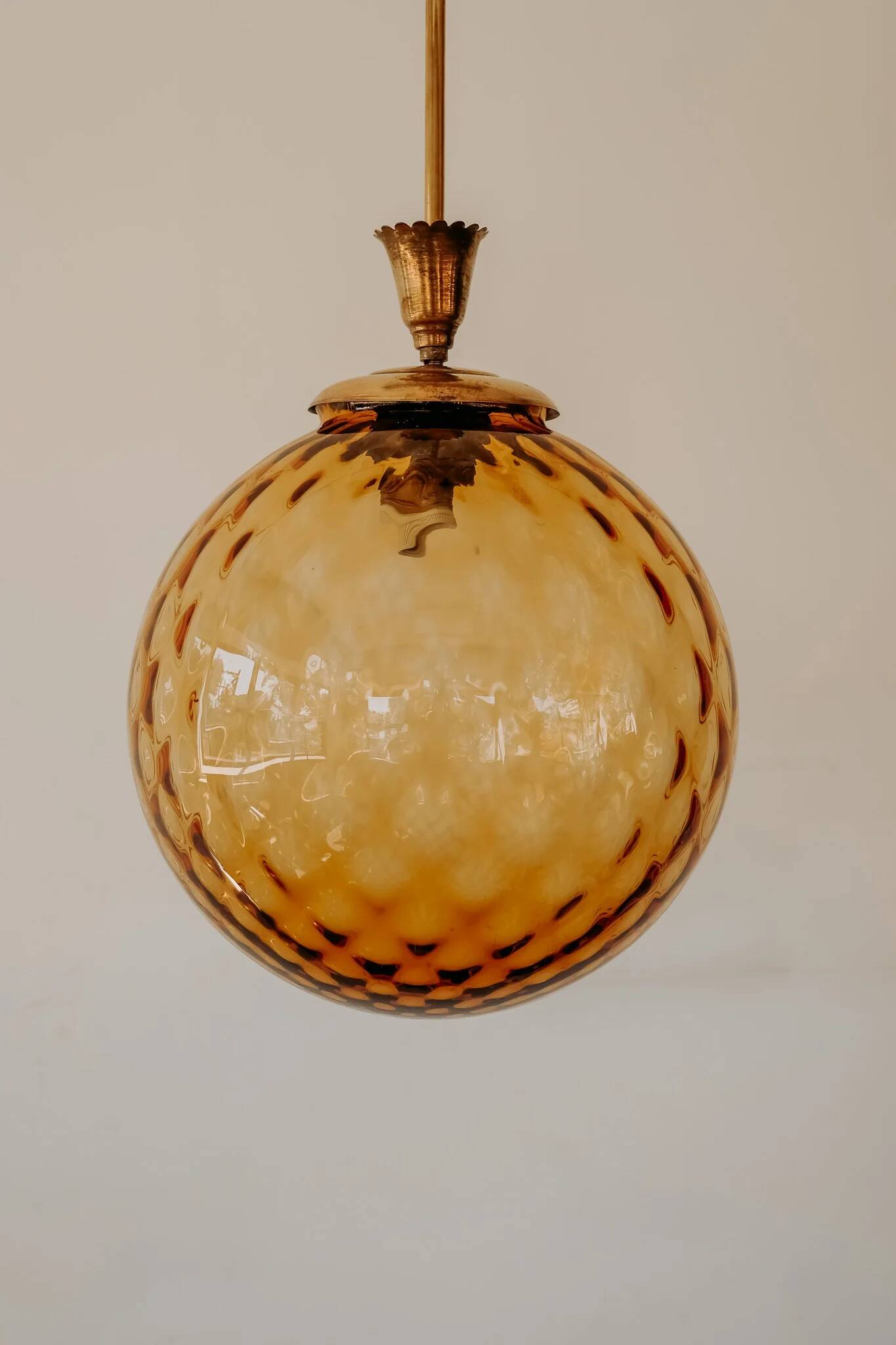 Brass pendant light with a round orange glass shade and a swirling structure.