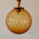Brass pendant light with a round orange glass shade and a swirling structure.