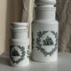 A pair of white glass bottles with Italian green patterns.