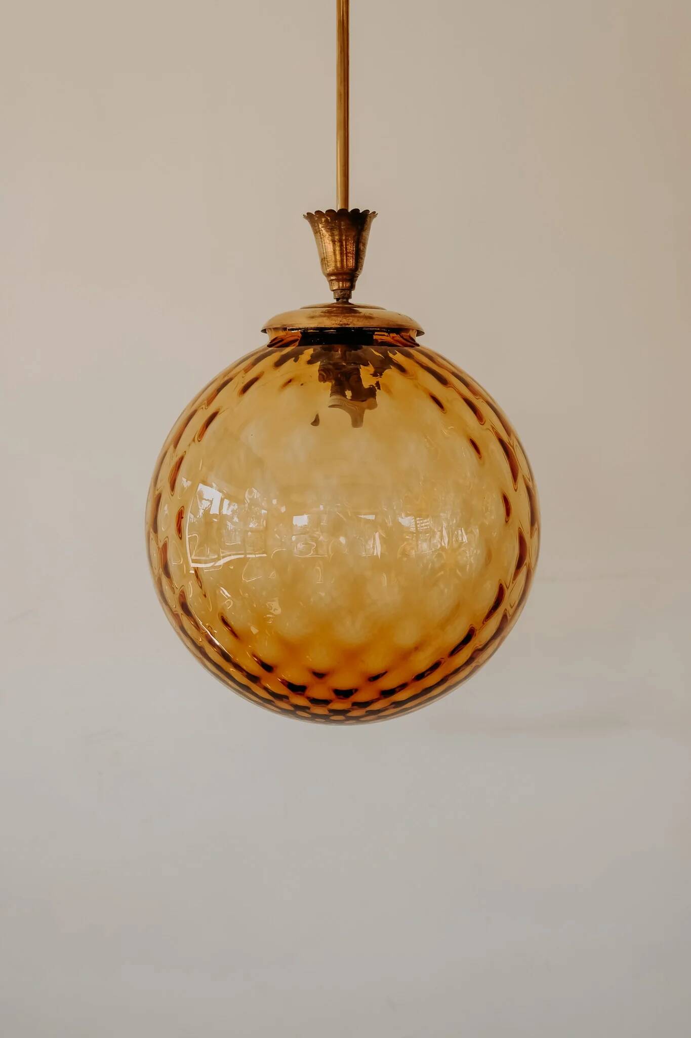 Brass pendant light with a round orange glass shade and a swirling structure.