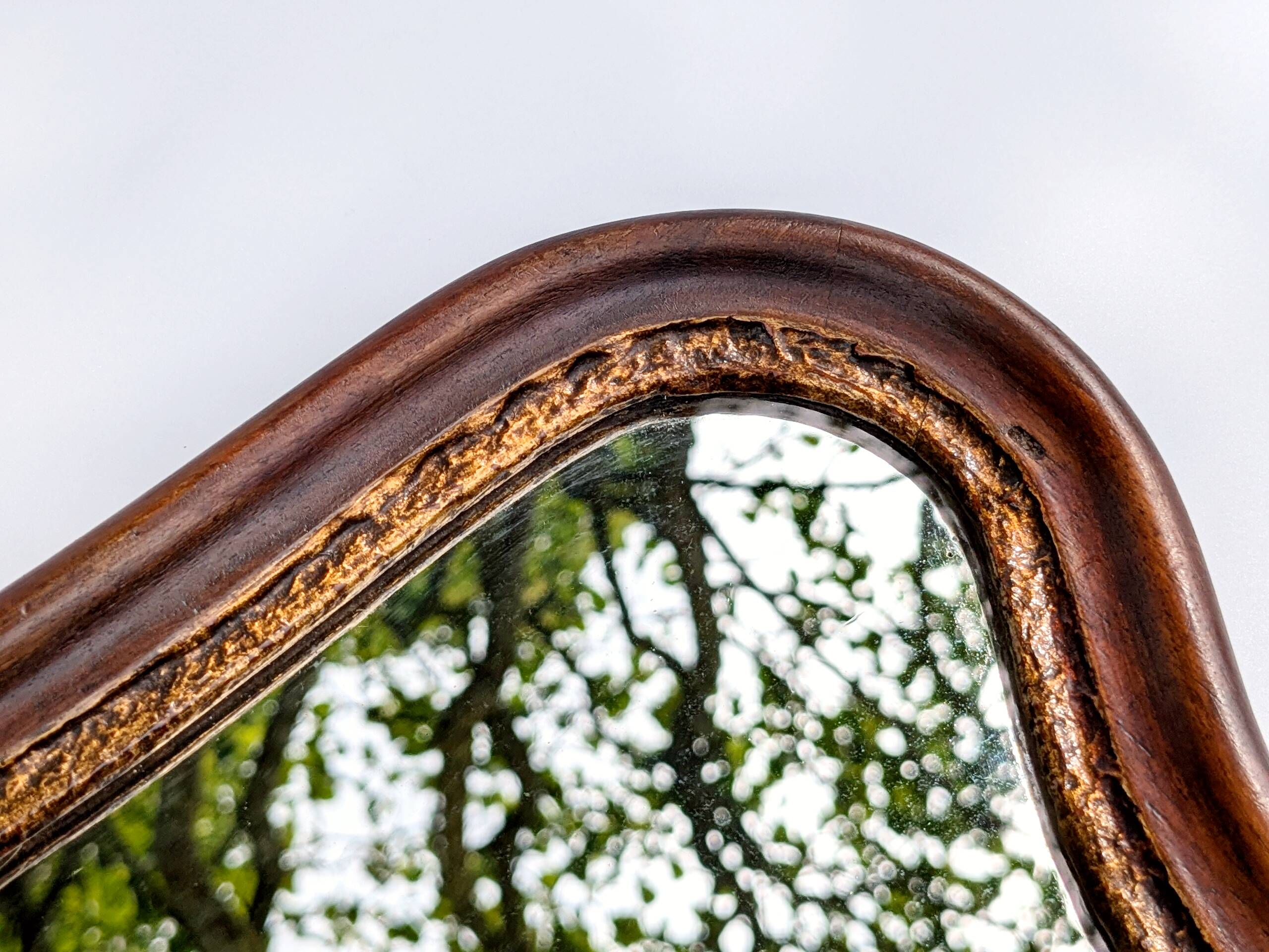 Antique wall mirror in carved wood with a wavy shape and a golden trim.
