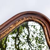 Antique wall mirror in carved wood with a wavy shape and a golden trim.