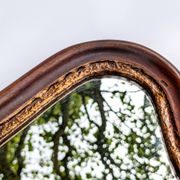 Antique wall mirror in carved wood with a wavy shape and a golden trim.