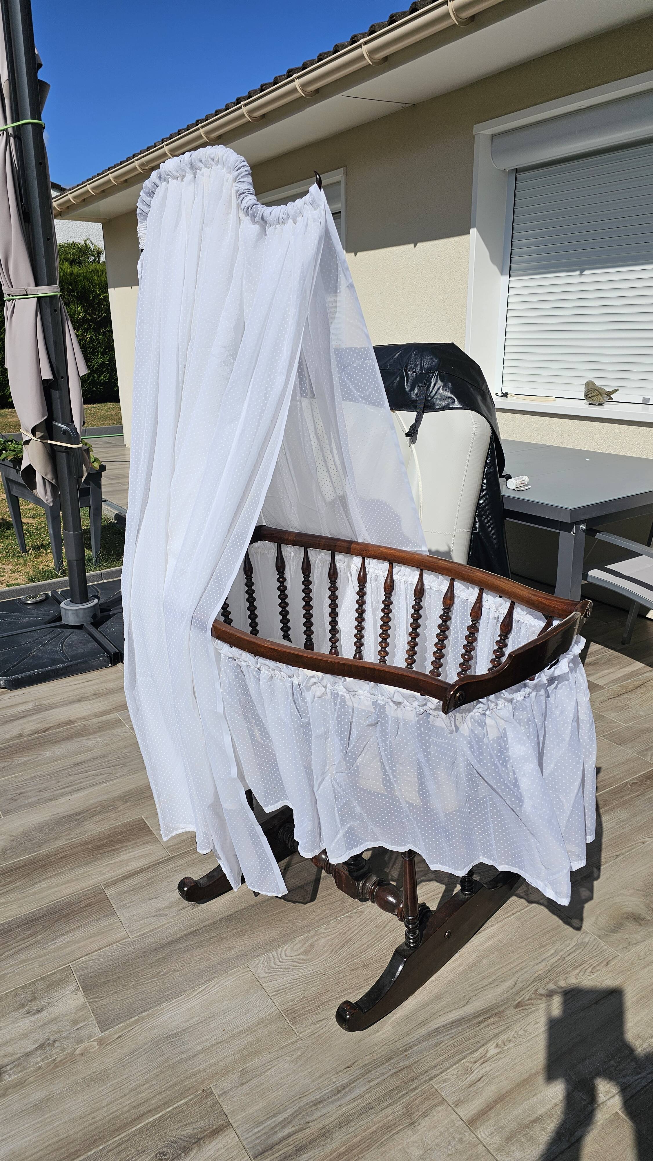 Old wooden rocking chair with turned legs and plumetis fabric.