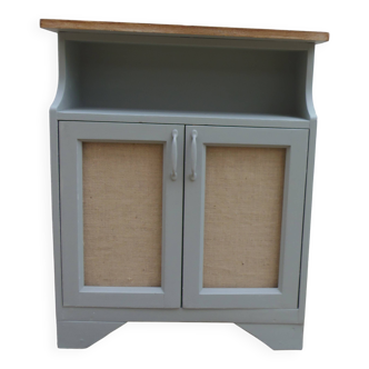 Small vintage green-grey piece of furniture, with 2 doors covered in burlap.