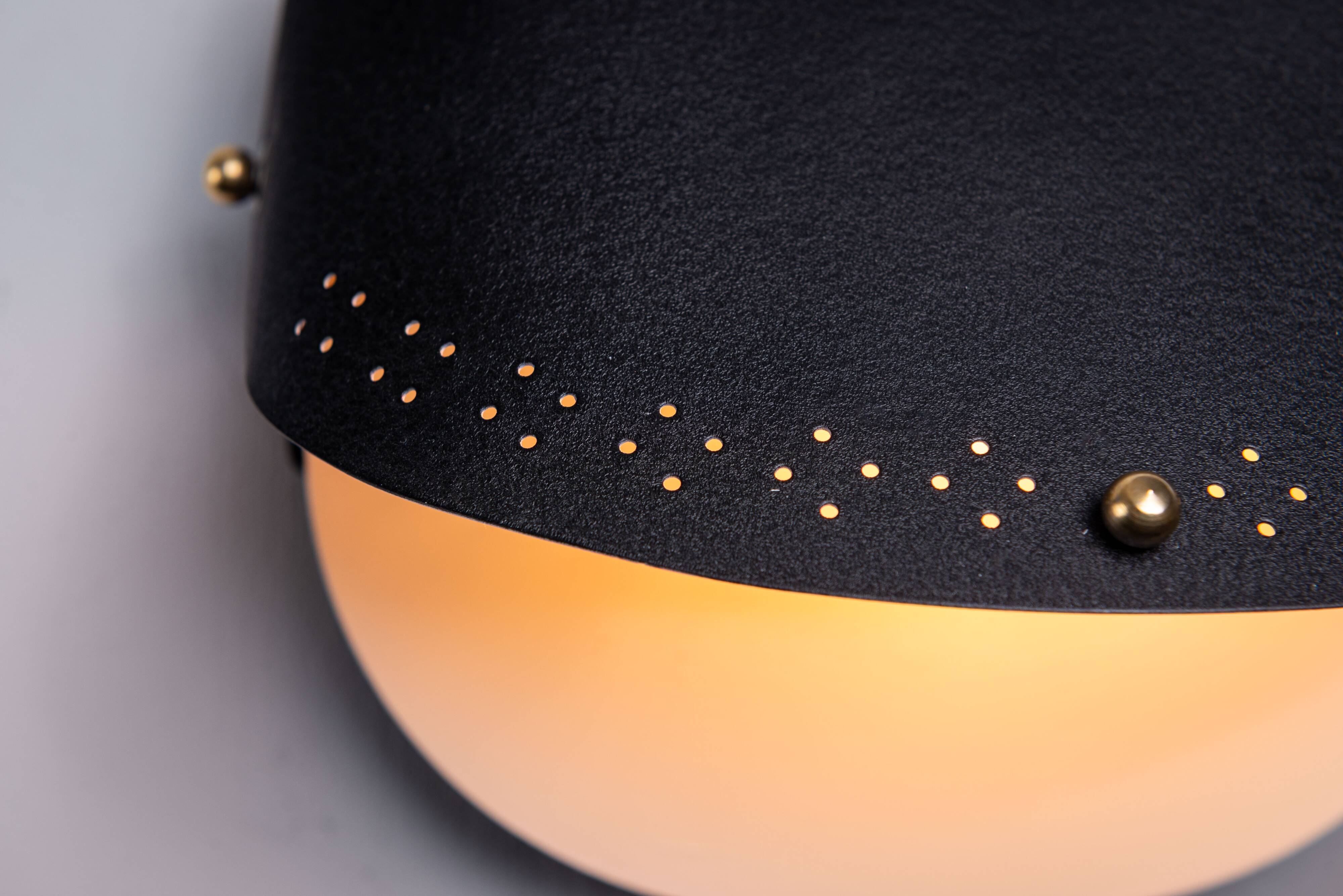 Matte black wall lamps with perforated shades and brass details