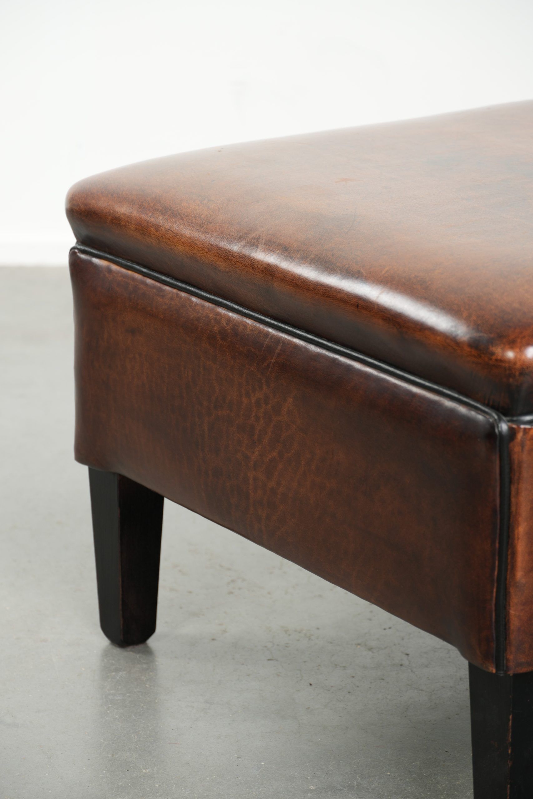Large dark brown square ottoman made of sheepskin with black piping