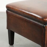 Pouf carré marron foncé en peau de mouton avec un passepoil noir.