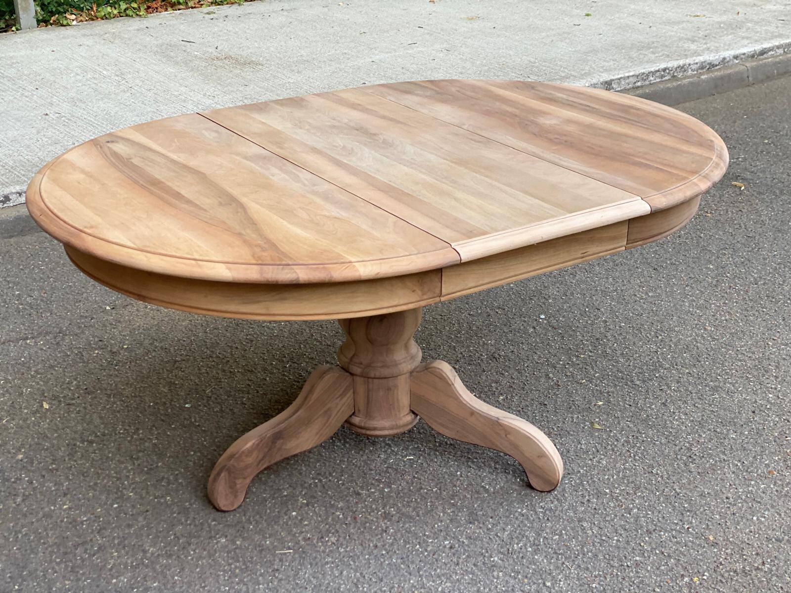 Round extendable dining table stripped in solid raw walnut with a central leg.