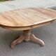 Round extendable dining table stripped in solid raw walnut with a central leg.