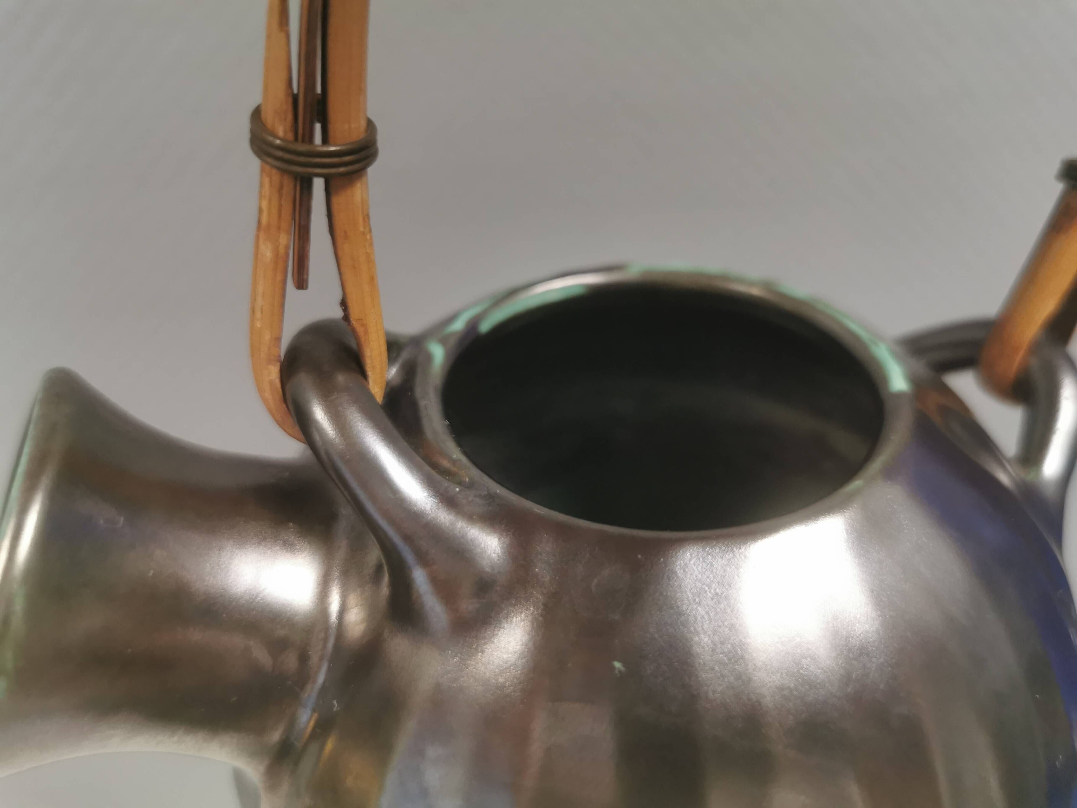 A ceramic jug with a metallic glaze and a handle made of woven raffia.