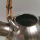 A ceramic jug with a metallic glaze and a handle made of woven raffia.