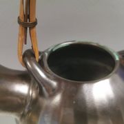 A ceramic jug with a metallic glaze and a handle made of woven raffia.