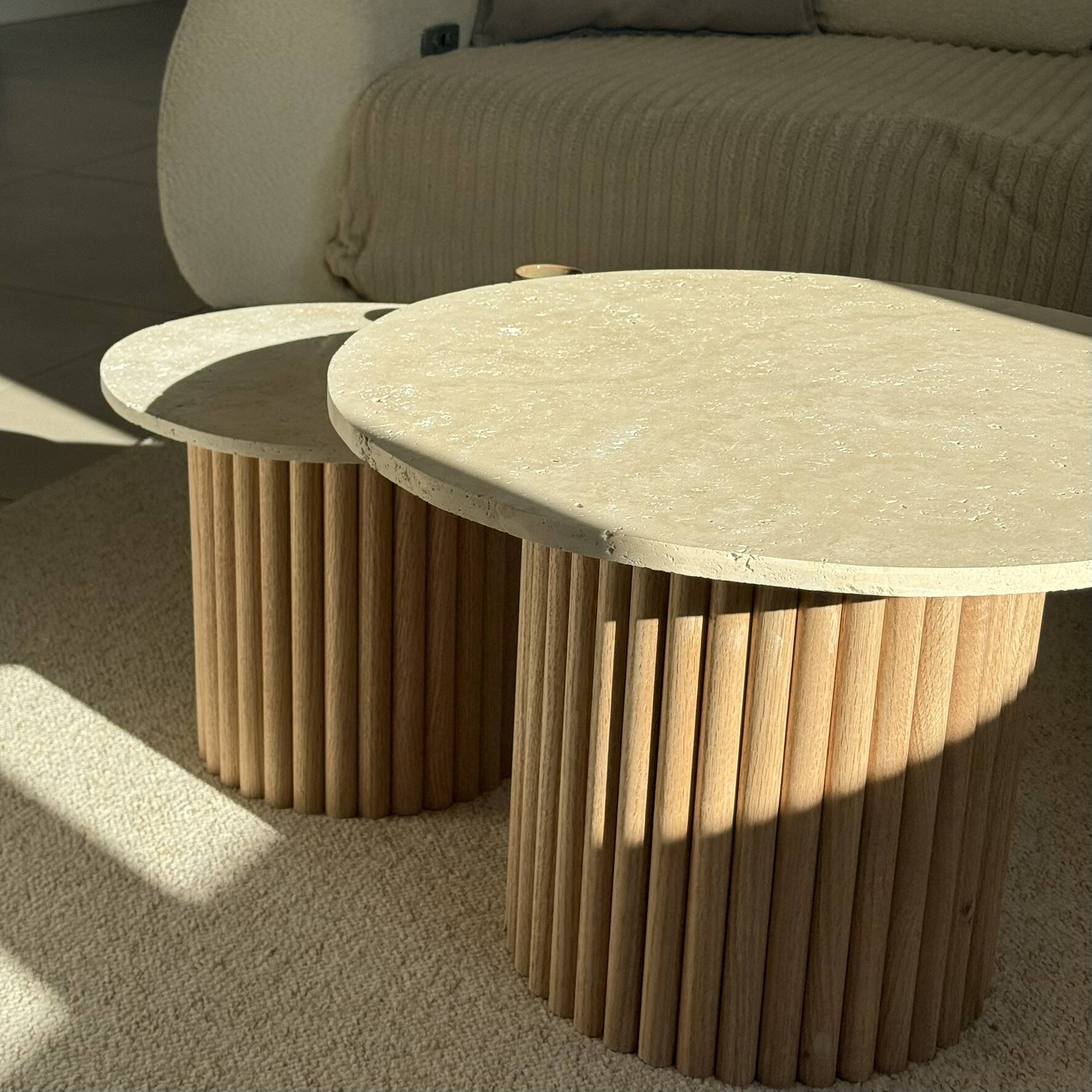 Round nesting coffee table in travertine and raw fluted wood.