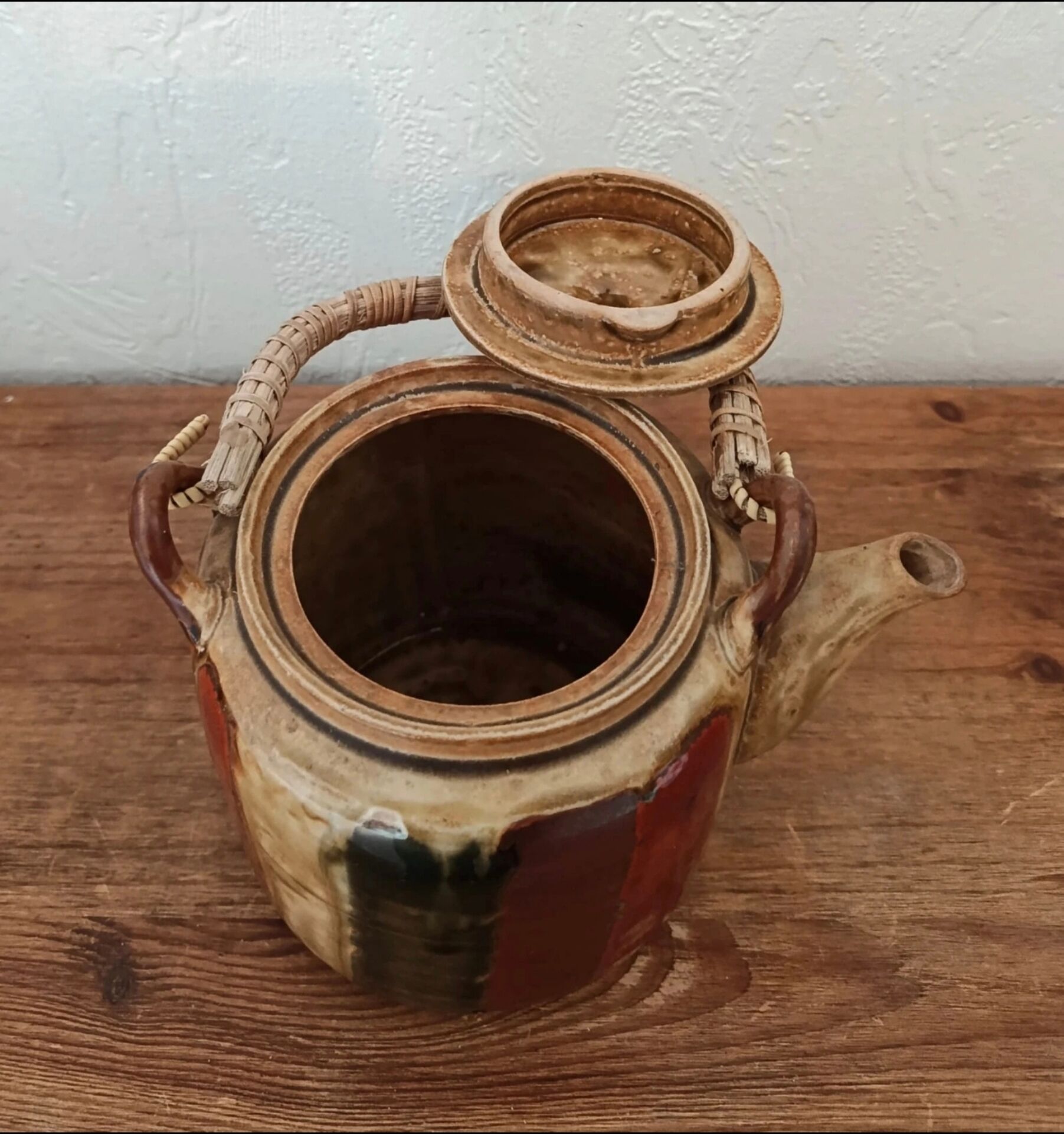 Vintage ceramic teapot with an enamel finish, rattan handle, warm tones.
