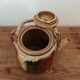 Vintage ceramic teapot with an enamel finish, rattan handle, warm tones.