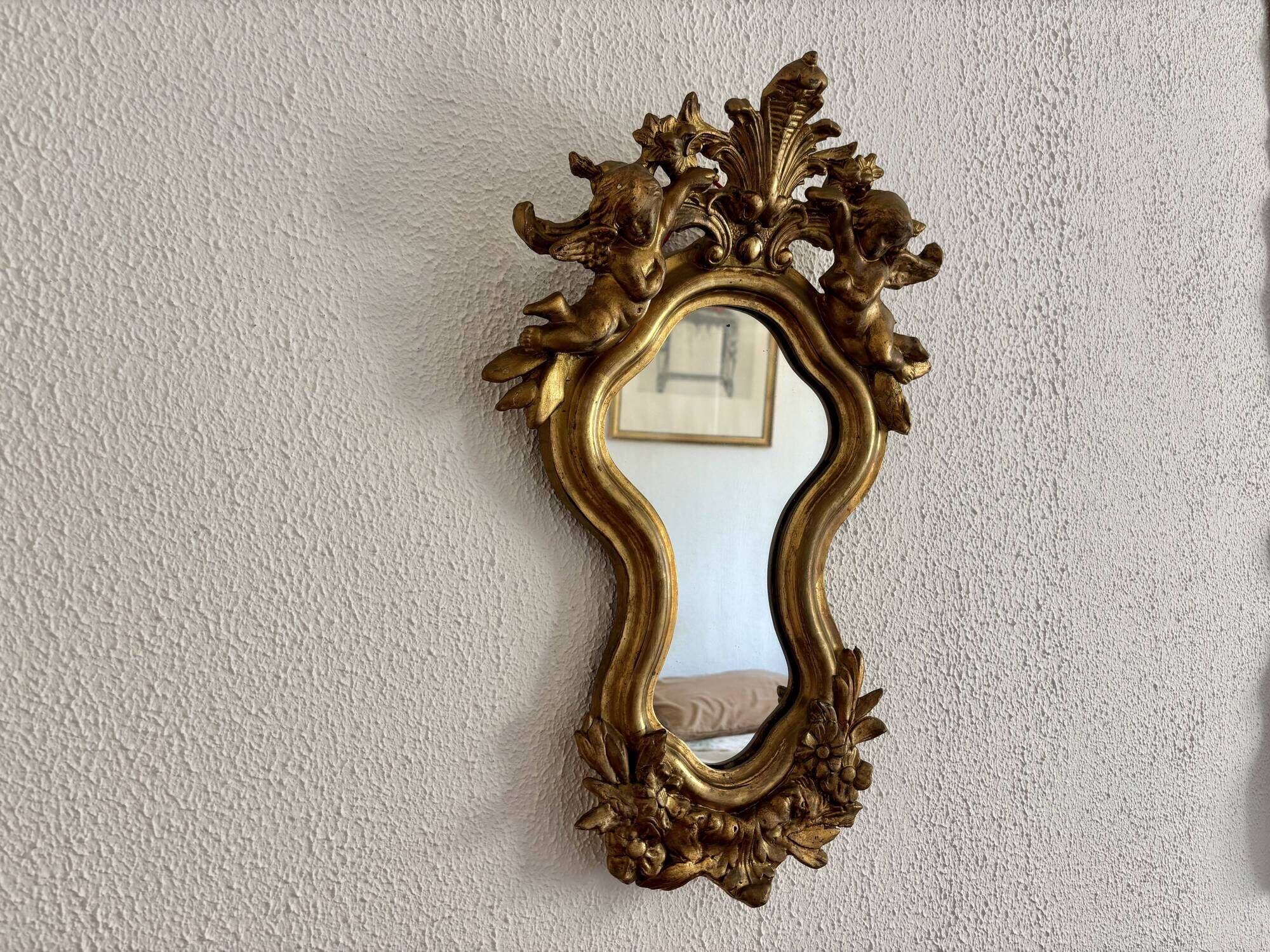 Antique rococo mirror with putti, gilded carved wood and stucco frame, 19th century.